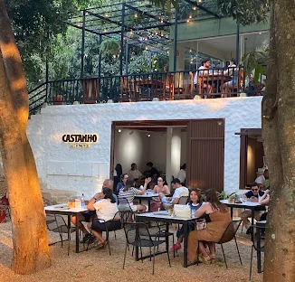 Fachada do Castanho na 108 Norte: o letreiro na parede branca, o mezanino com varal de luzes e as mesas ocupadas sob as árvores